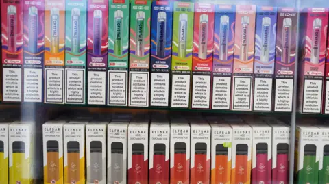 A line of colourful boxes on a shelf containing various vapes of different flavours