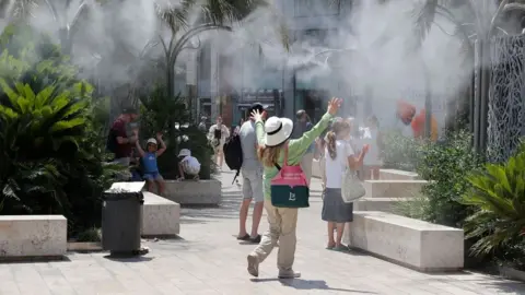 Tourists cool off under a cloud of mist in Valencia, Spain on Sunday