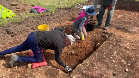 Volunteers wearing gloves working on the dig site at High Tarns Farm, Silloth.