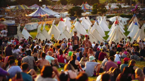 A crowd of Glastonbury goers sat on the hill overlooking the festival site.
