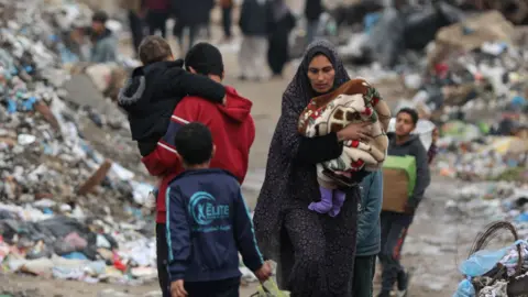 Palestinians walking along a path covered in piles of rubbish.