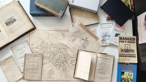 Derby City Council A view of historical documents on a table used to help create Darbye. Visible are maps, pamphlets, and books.