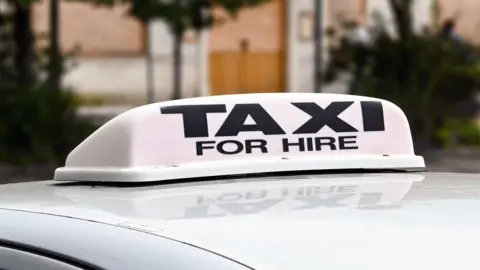 Getty Images A silver car with a "Taxi for hire" sign on the top of it.