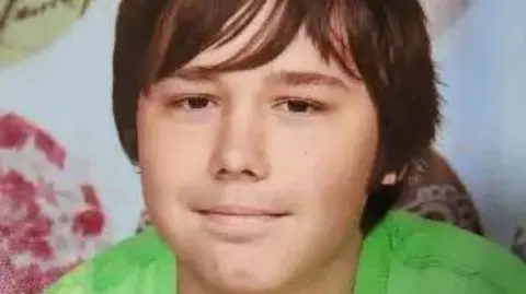 A man smiling looking at the camera. He is wearing a green T-shirt and has brown hair. 