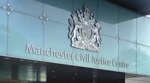 An exterior shot of the Manchester Civil Justice Centre sign. Above the silver text is the city's crest.