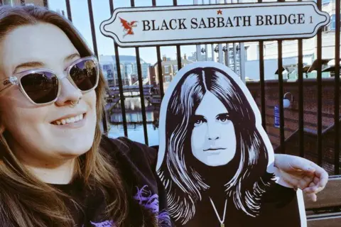 Kirsty Boswell A dark-haired woman wearing dark glasses sits with her arm around an image of Ozzy Osbourne