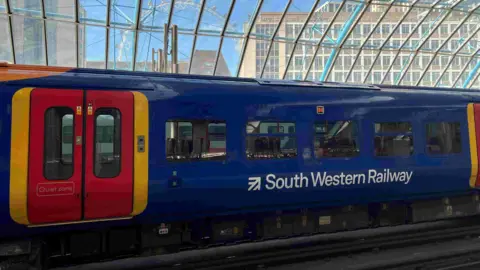 An SWR train at London Waterloo in blue, red and yellow colours. The London Eye is visible through the glass roof of the station.