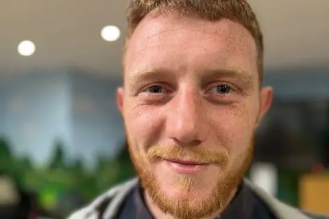 Man with a beard and red hair, smiling in a room.