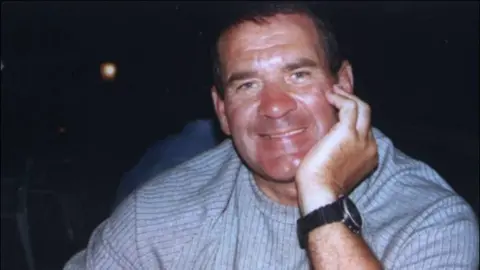 Supplied Michael Steele is wearing a grey jumper and leaning on his hand. He is smiling and wearing a black watch on his wrist.