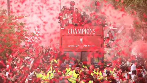 EPA Liverpool players on their open top bus shrouded in red flare smoke with people packing the streets