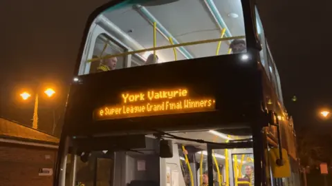 A double decker bus on a dark evening. At the front of the bus it reads: York Valkyrie Super League Grand Final Winners