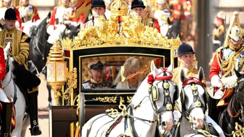 Getty Images King Charles and Queen Camilla leave Buckingham Palace in the horse-drawn Diamond Jubilee State Coach to travel to the Palace of Westminster to deliver the King's Speech as part of the State Opening of Parliament on 17 July, 2024. The Royal couple are pictured through the glass front of the carriage, surrounded by uniformed footmen and officers on horseback. 
