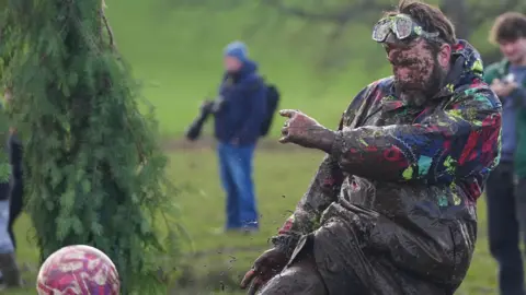PA Media A player is volleying the football and coated in dark mud. He has goggles resting on his head 