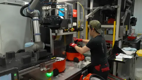 Man working on machine wearing a green baseball cap backwards.