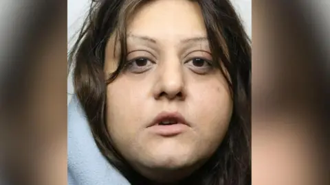 Sidrah Nosheen's custody image, where she is looking at the camera with a blank expression and has very thin, overplucked eyebrows and dark messy hair. She appears to be wearing a grey hoodie. 