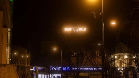 ACJ Media A sign on top of a building in Derby city centre at night which reads COOP MILK