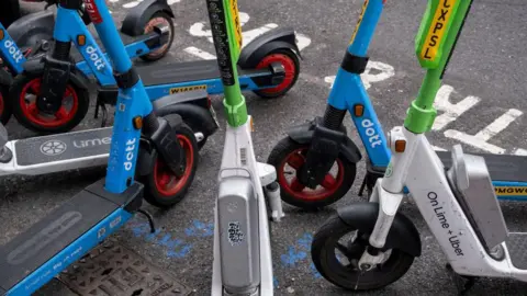 Cropped picture of several branded e-scooters parked on the side of the road