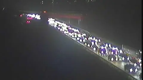 A view of the M1 motorway during a closure. Heavy traffic can be seen on one side of the carriageway while the other is empty. It is dark and cars have their headlights on.