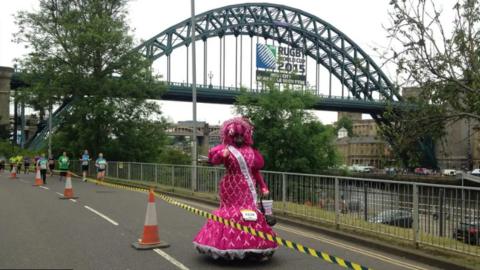 Colin Burgin-Plews in a very large pink dress running along the quayside 