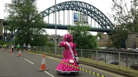 Colin Burgin-Plews Colin Burgin-Plews in a very large pink dress running along the quayside 