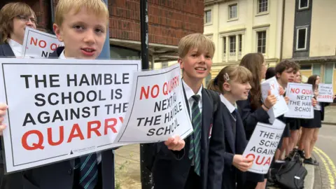 Children in school uniform hold signs saying "The Hamble School is against the quarry"