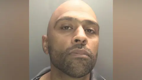 Zaynul Shaffi pictured in a mugshot. He is bald and has a dark stubble beard.

