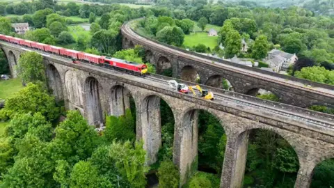 Network Rail A train passing two diggers on the platform of a tall viaduct