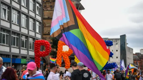 Pacemaker A large pride flag being flown above a crowd of people. 