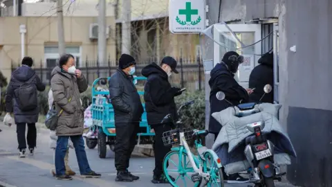 EPA-EFE/REX/Shutterstock People wearing masks queuing outside a pharmacy