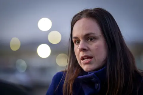 PA Media Kate Forbes is mid-speech and wears a dark blue jacket. She has long dark brown hair and the background is blurred
