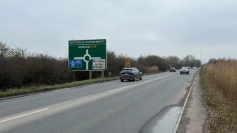 The A38, there are cars on both sides of the road and there is a sign signalling the approach of Edithmead roundabout.