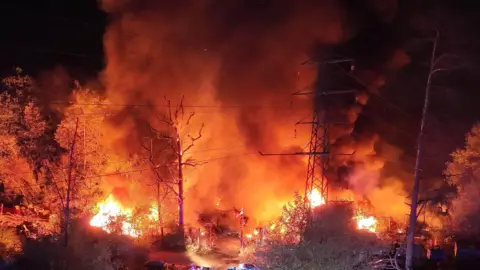 A large fire at night-time with orange flames and power cables