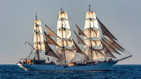 Light-coloured tall ship with masts and beige sails in the sea.