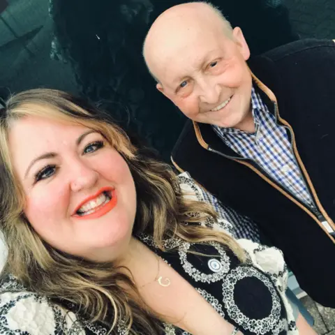 Bucket List Wishes Gini Hackett on the left with highlighted hair and black and white dress. She is smiling at the camera. To her right is Glen Edwards wearing a checked shirt also smiling at the camera.