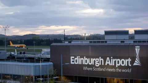 Getty Images Exterior shot of Edinburgh Airport with signage reading "Where Scotland meets the world" and in the background an orange airplane on the runway