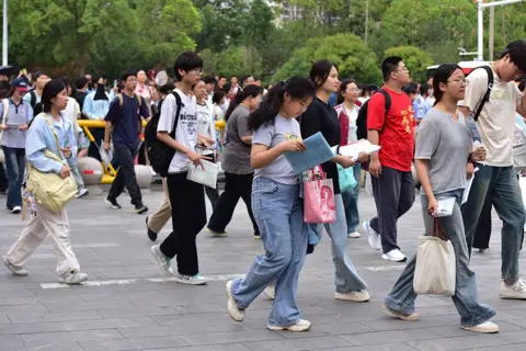 Getty Images A girl reads a book while she walks with a dozen high school graduates into an exam venue for Gaokao this year