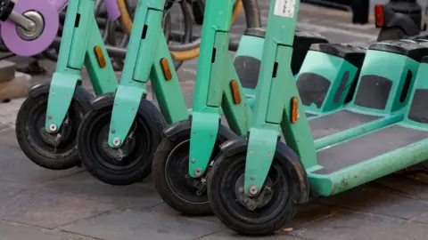 A close-up of a row of e-scooters stood in a row on a pavement