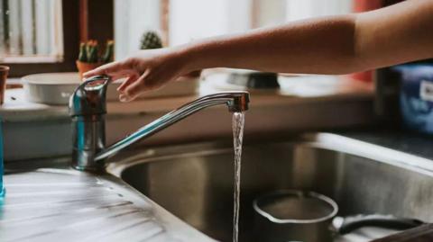 A person touching a tap while water pour into a sink