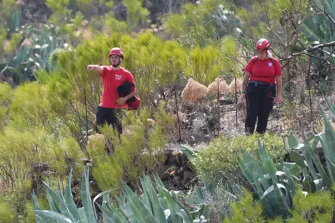 PA Media A man and a woman wearing dark trousers and red t shirts stand among the terrain in Tenerife.