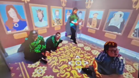 Greenfield Special School A picture of the immersive room being used in an educational lesson at Greenfield school. There are three students and a teacher inside. The two walls have portraits of kings and queens on. The floor is also lit up with yellow flowers and various moving patterns.