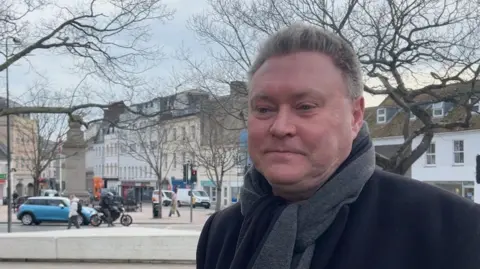 Deputy Rob Ward is wearing a black coat and has a grey scarf. 