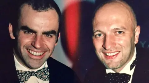 Tony Jones Tony Jones, who has short black hair, stands next to Bryan Gunn. Both are wearing white shirts and bow ties and are smiling.