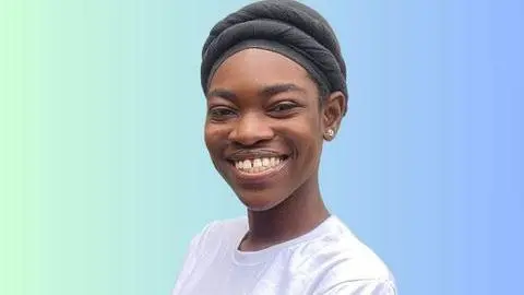 Saviour Iwezue, in a white T-shirt and black headscarf, gives a beaming smile to the camera. Her background goes from green on the left, to blue on the right.