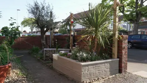A small outdoor space at the front of a house with a raise gardening bed. 