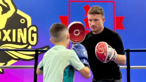 EMPIRE FIGHTING CHANCE Boxer Dalton Smith wears pads on his hands as he coaches a young boxer in the ring.