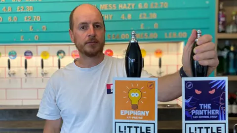 Matthew Willers, standing behind a bar, holding one of the beer pumps