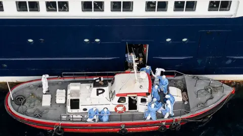 Getty Images Aerial view shows health personnel assisting patients onto a boat from the cruise ship MV Hondius, while stationary off the port of Praia, the capital of Cape Verde.