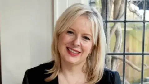 Getty Images A head and shoulders image of Allison Pearson smiling at the camera, wearing a black dress or top, with a window behind her 