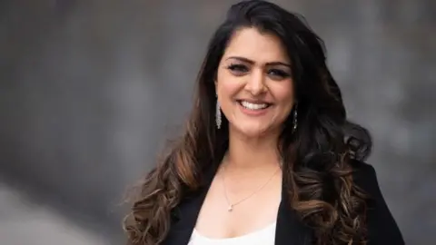 Getty Images Natasha Asghar smiling to the camera with a blurred image of the wall of the Senedd building behind her