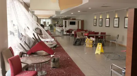 A picture showing damage inside the hotel which shows smashed glass across the floor with upturned chairs
